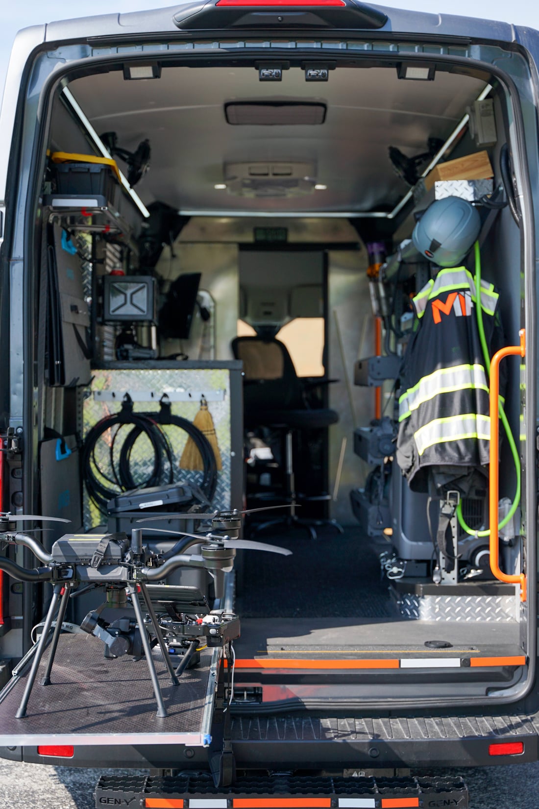 Rear of the MIR command van showing the drone on the deployment ramp, organized equipment, and the MIR-branded safety vest and helmet