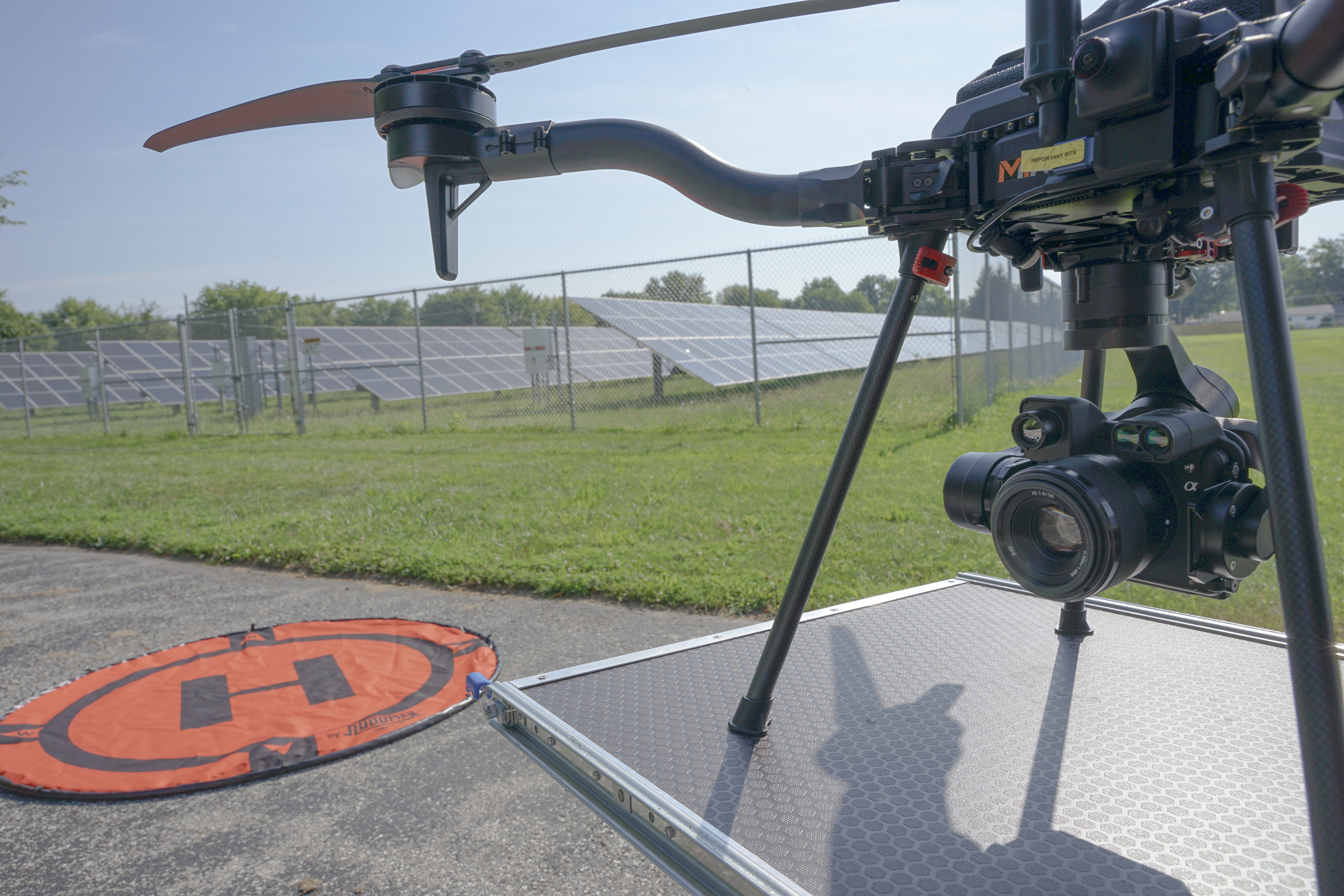 MIR Freefly Astro with the Sony RGB camera and laser rangefinder payload staged on a loading ramp beside an orange landing pad, with a ground-mounted solar array in the background