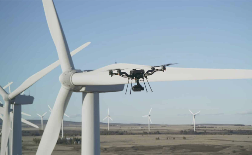 American-made Freefly Astro drone hovering alongside a wind turbine blade during an autonomous inspection pass, with a field of turbines under a clear sky behind it